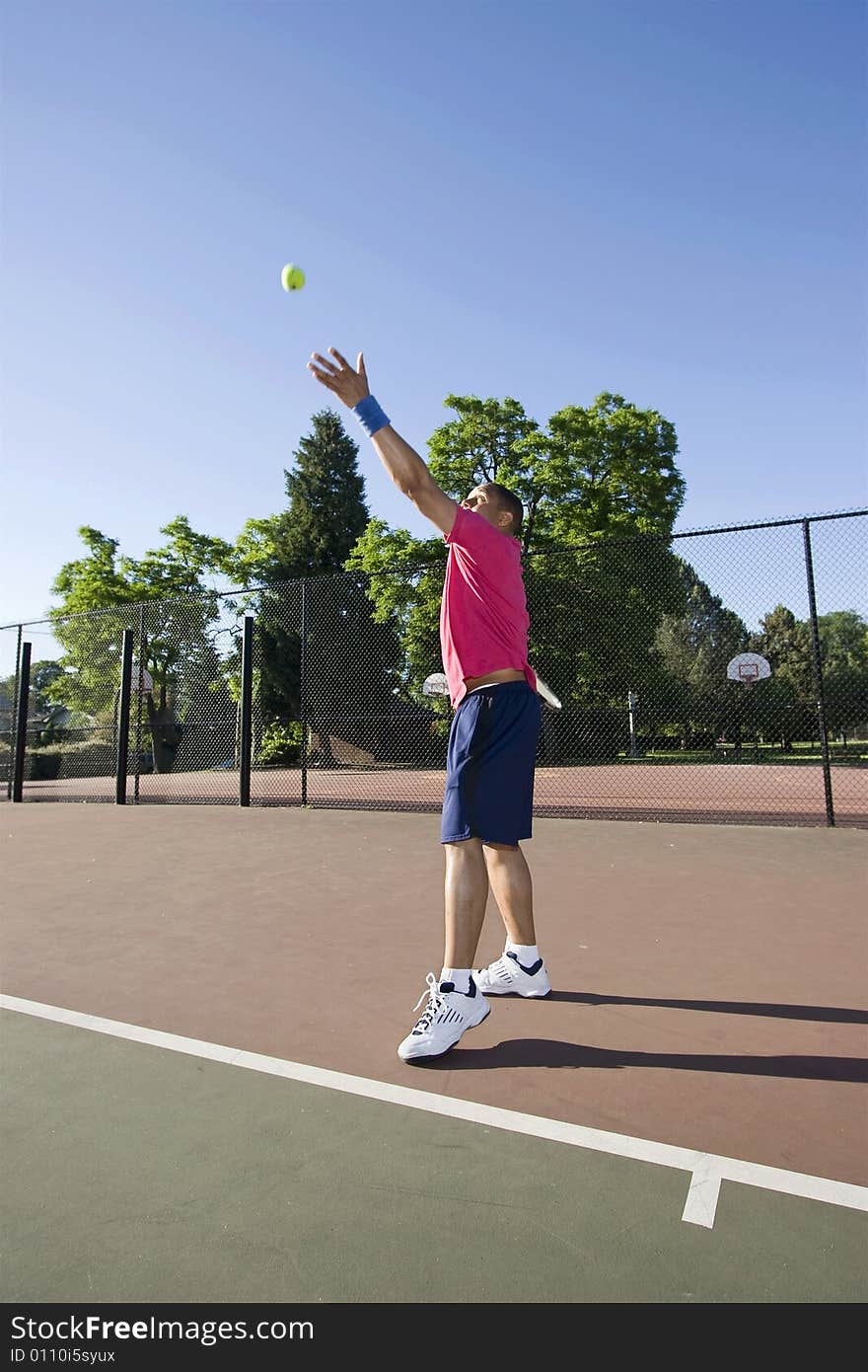 A man is outside on a tennis court playing tennis.  He is about to serve and looking at the ball in the air.  Vertically framed shot. A man is outside on a tennis court playing tennis.  He is about to serve and looking at the ball in the air.  Vertically framed shot.