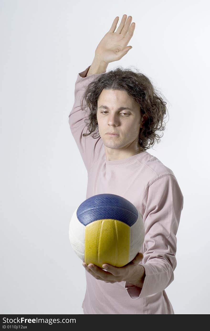 Man holds a volleyball in one hand and raises his other hand to serve it. Vertically framed photograph. Man holds a volleyball in one hand and raises his other hand to serve it. Vertically framed photograph