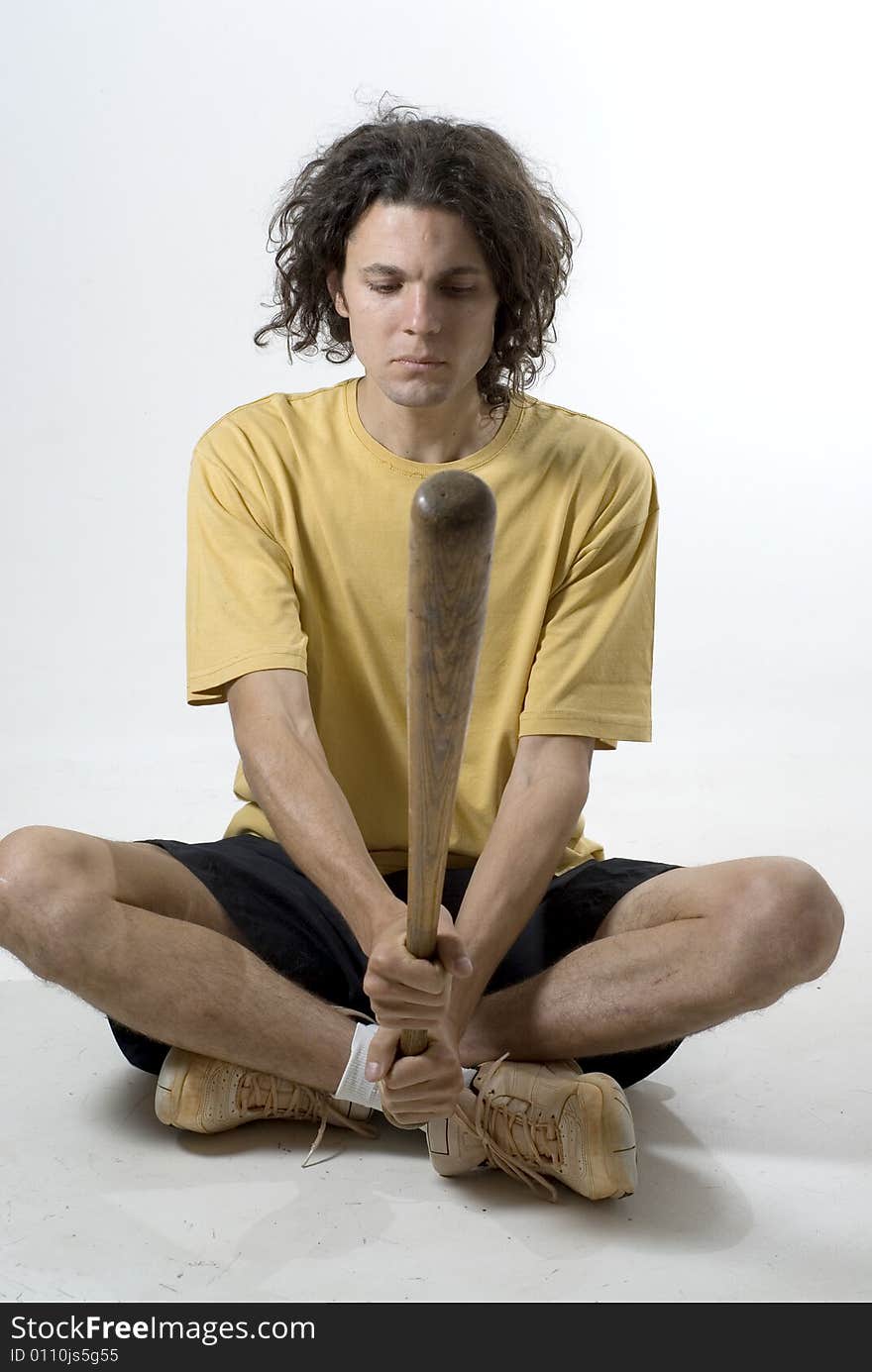 A man holding a  baseball bat and sitting on the floor. Vertically framed photograph. A man holding a  baseball bat and sitting on the floor. Vertically framed photograph