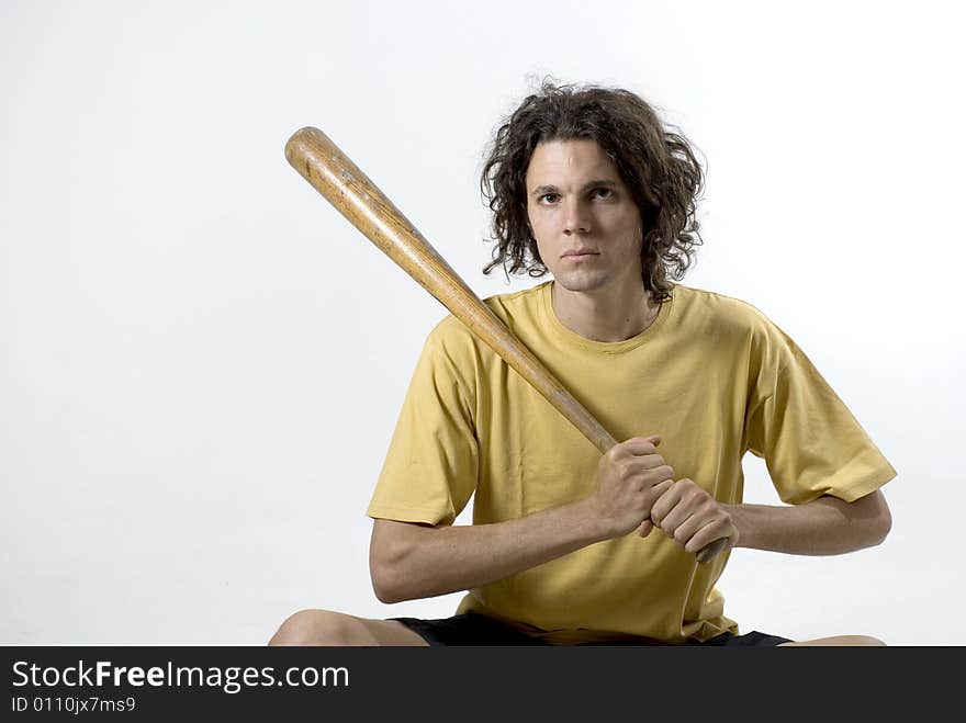 A man holding a baseball bat and sitting on the floor with a serious look on his face. Horizontally framed photograph. A man holding a baseball bat and sitting on the floor with a serious look on his face. Horizontally framed photograph