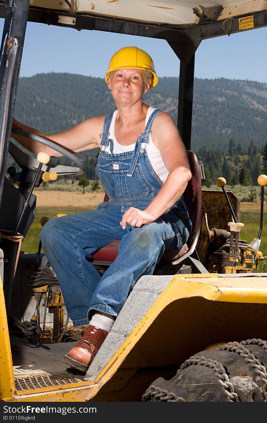 Senior woman on backhoe wearing yellow hardhat. Senior woman on backhoe wearing yellow hardhat