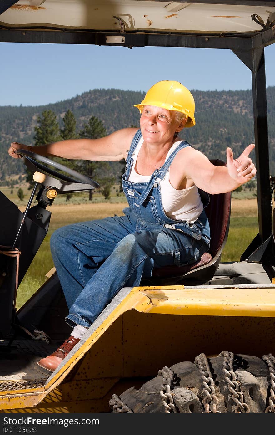 Senior woman on backhoe wearing yellow hardhat. Senior woman on backhoe wearing yellow hardhat