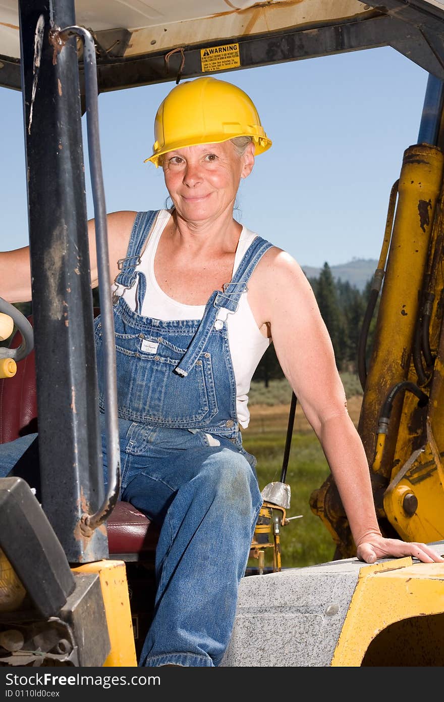 Senior woman on backhoe wearing yellow hardhat. Senior woman on backhoe wearing yellow hardhat