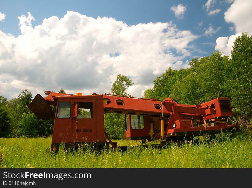 Large red excavator in a green field under a blue sky. Large red excavator in a green field under a blue sky.