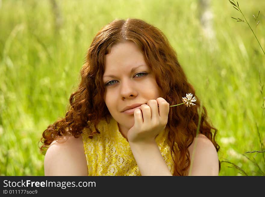 The beautiful girl sits on a background of a lawn. The beautiful girl sits on a background of a lawn