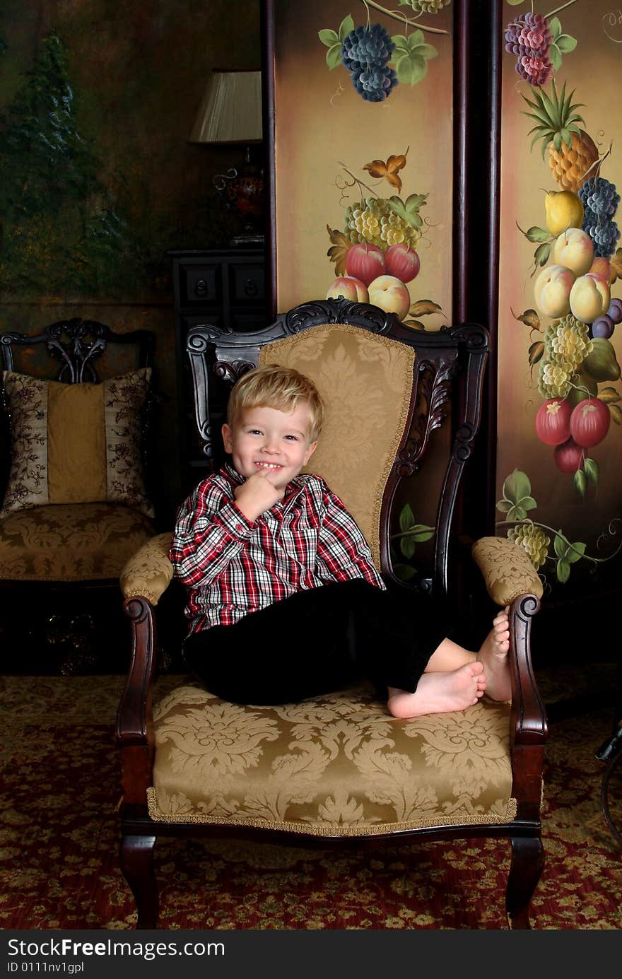 Boy sitting on an antique chair in red plaid shirt and black corduroy winter pants. Boy sitting on an antique chair in red plaid shirt and black corduroy winter pants