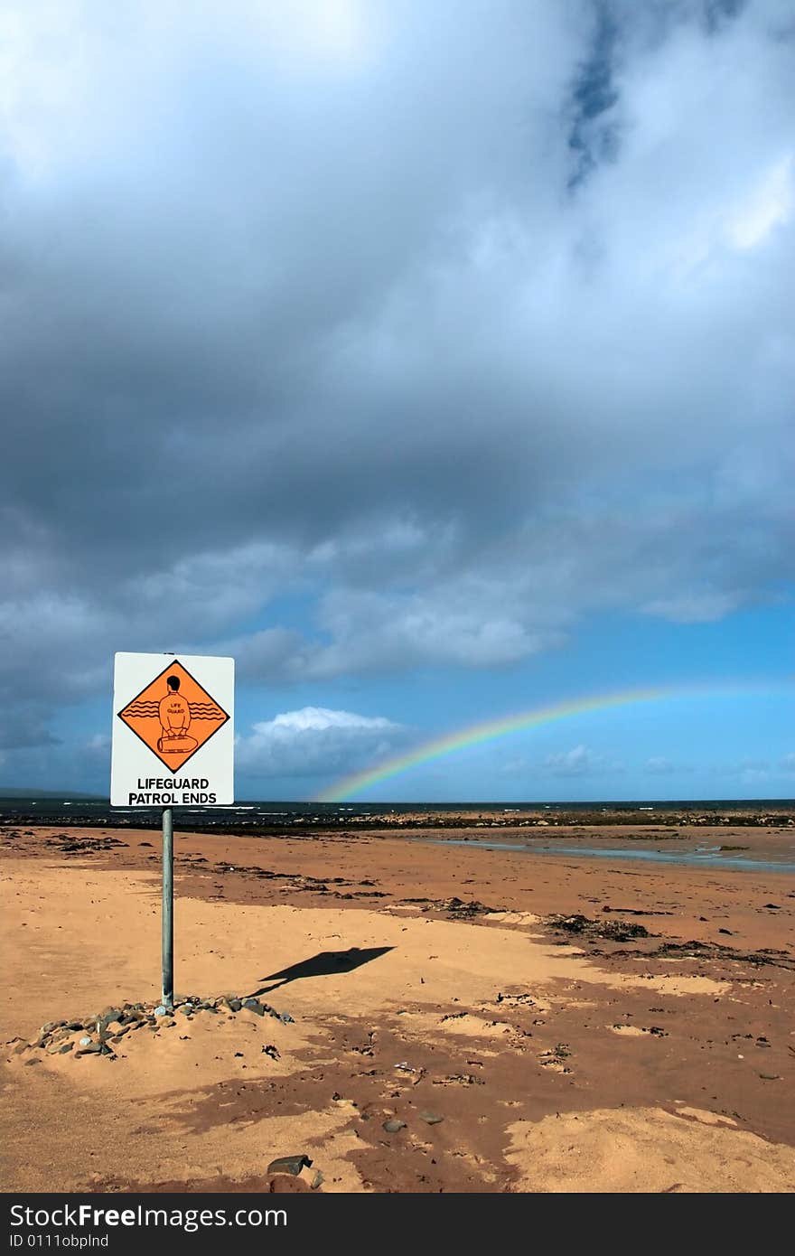 A sign warning that there is no lifeguard patrol beyond this sign with a beautiful rainbow in the background. A sign warning that there is no lifeguard patrol beyond this sign with a beautiful rainbow in the background