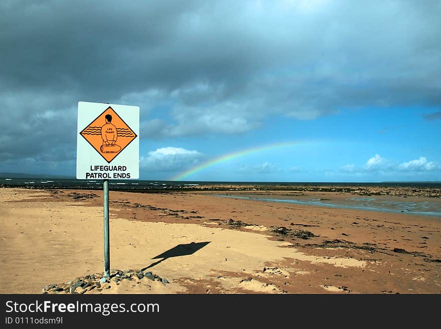 A sign warning that there is no lifeguard patrol beyond this sign with a beautiful rainbow in the background. A sign warning that there is no lifeguard patrol beyond this sign with a beautiful rainbow in the background