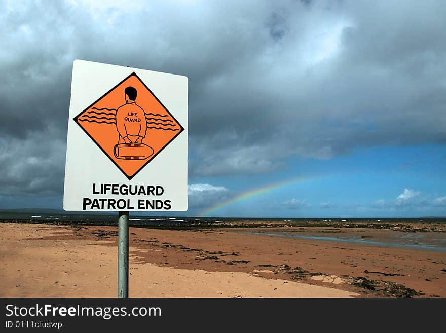 A sign warning that there is no lifeguard patrol beyond this sign with a beautiful rainbow in the background. A sign warning that there is no lifeguard patrol beyond this sign with a beautiful rainbow in the background