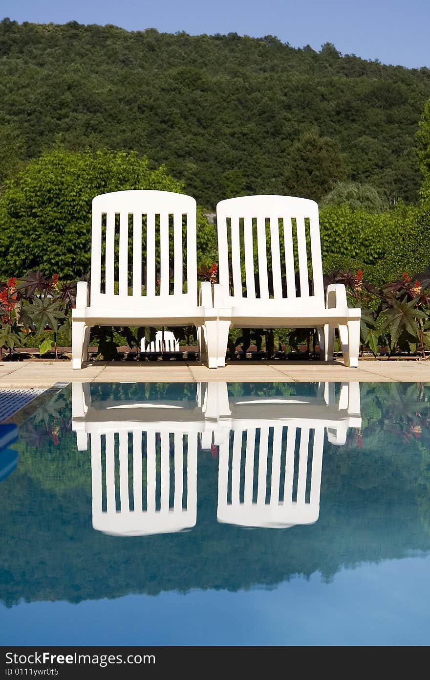 Two white sunloungers reflected in a blue swimming pool. Two white sunloungers reflected in a blue swimming pool