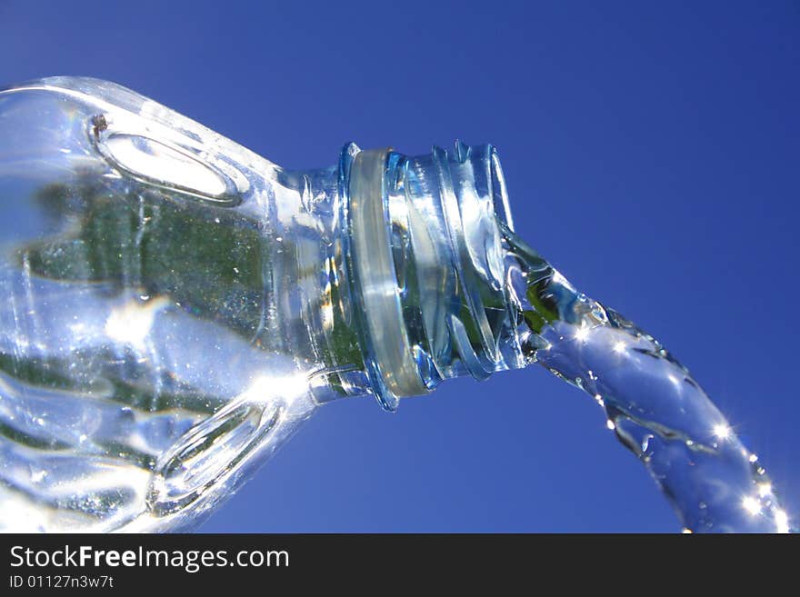 Beautiful clear water flows from a bottle against a blue sky. Beautiful clear water flows from a bottle against a blue sky