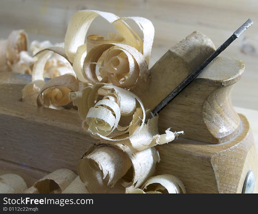 A plane with freshly carved strand on a plank of wood. A plane with freshly carved strand on a plank of wood