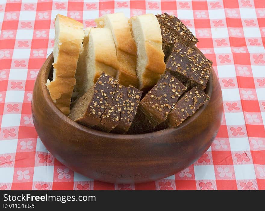 Slices of wheat and rye bread in a wooden bowl on a table covered with checkered buckram