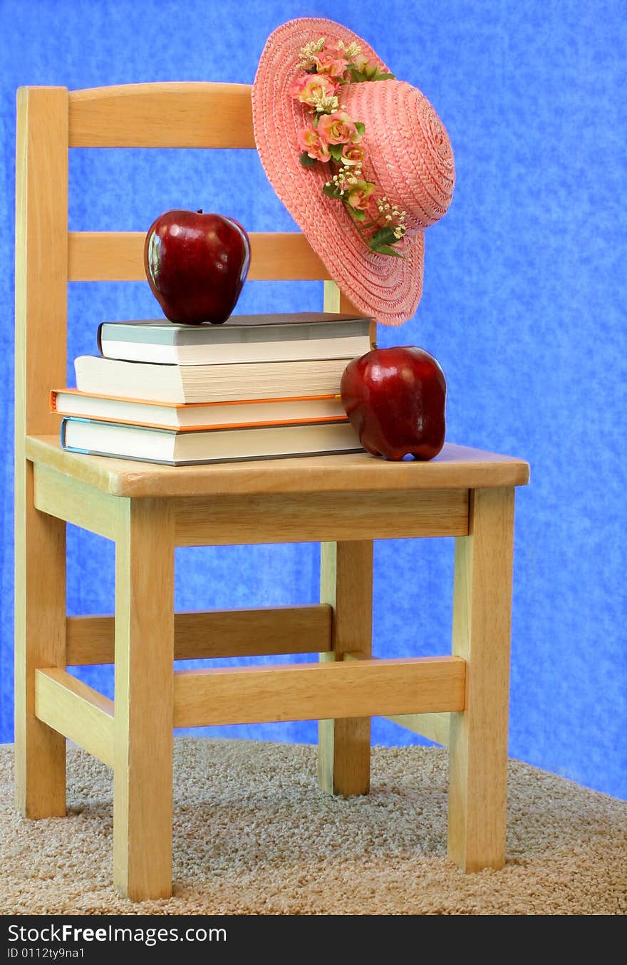 Vintage child's school chair with books, apples and a little girls hat. Vintage child's school chair with books, apples and a little girls hat.