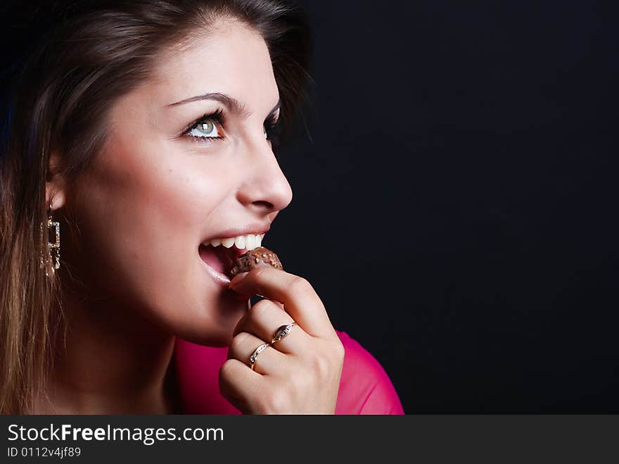 Portrait of beautiful girl in a pink woman's jacket with a chocolate candy in the mouth