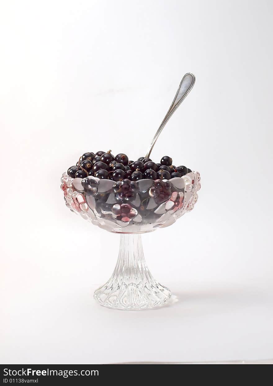 Berries of a black currant lay in a glass vase on a white backgroun