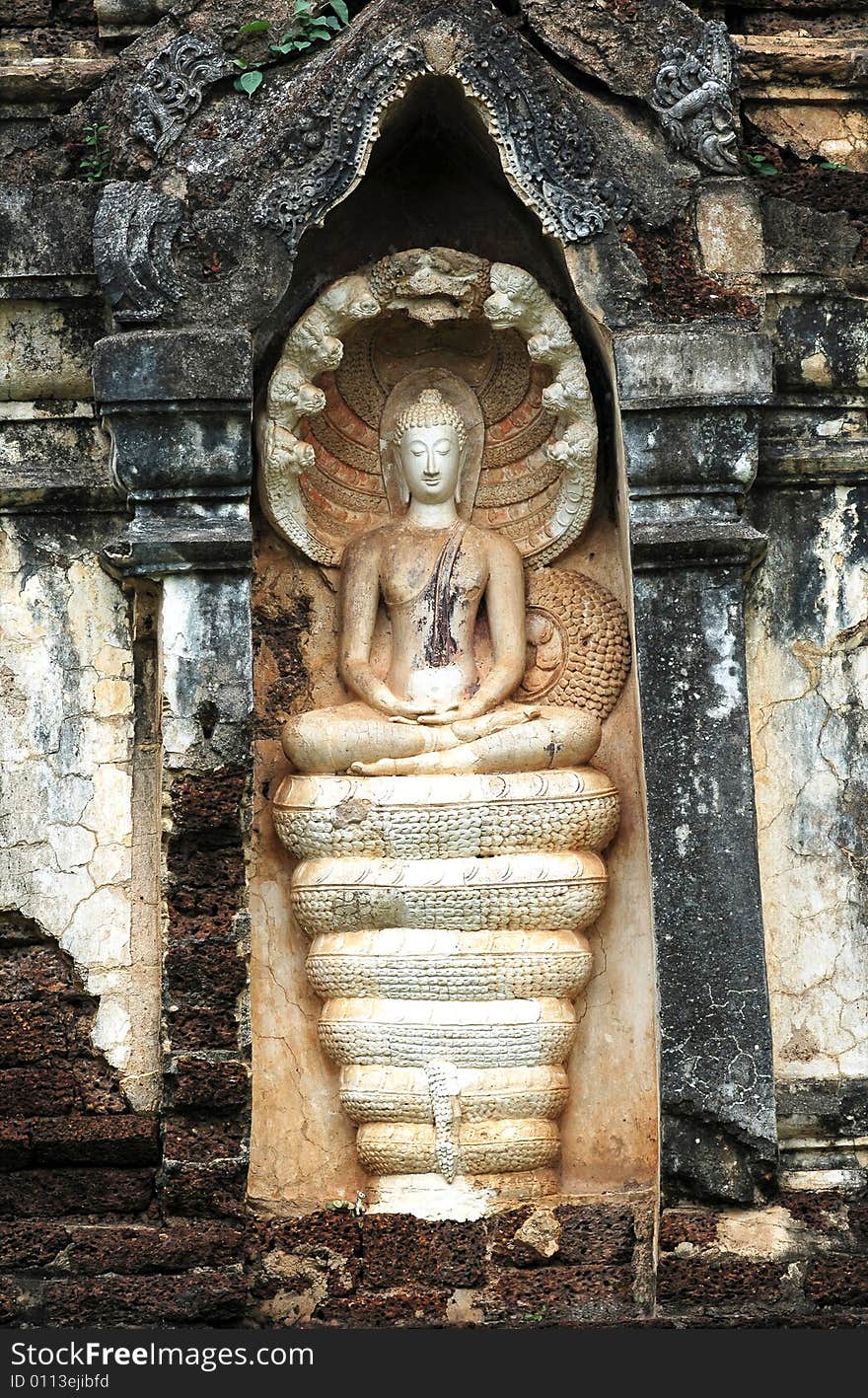 Thailand, Sri Satchanalai historical park; Detail of a carved wall with a seated Buddha protected by the seven head Khmer naga. Thailand, Sri Satchanalai historical park; Detail of a carved wall with a seated Buddha protected by the seven head Khmer naga