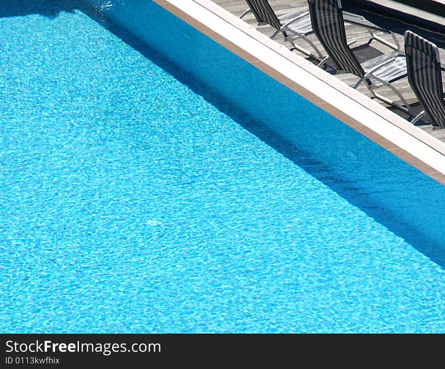 A pool with blue water and some decks chair in the solarium. A pool with blue water and some decks chair in the solarium