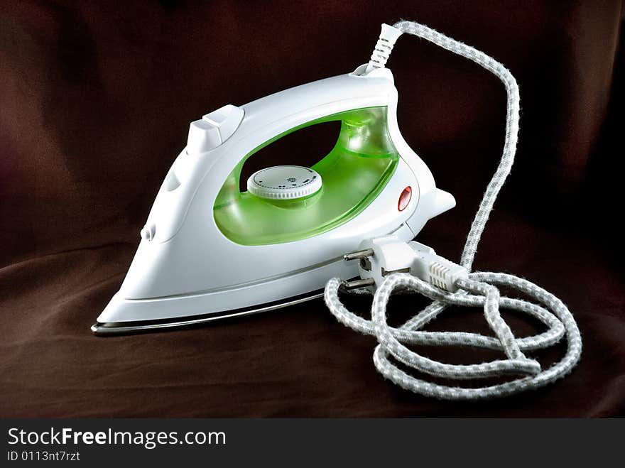 The electric iron stands on a brown background