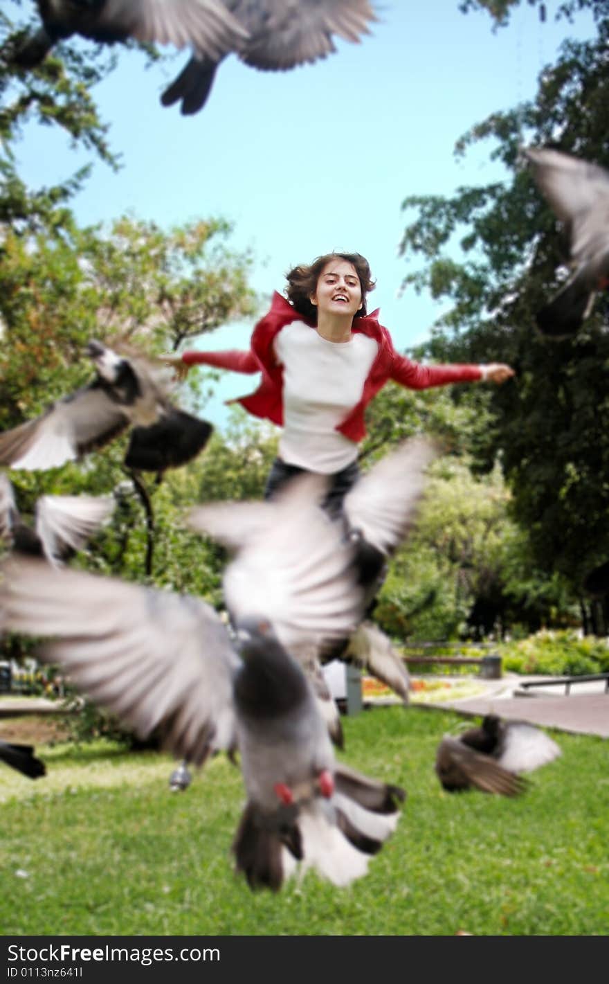 Smiling woman in a park, chazing pigeons with scattered hands