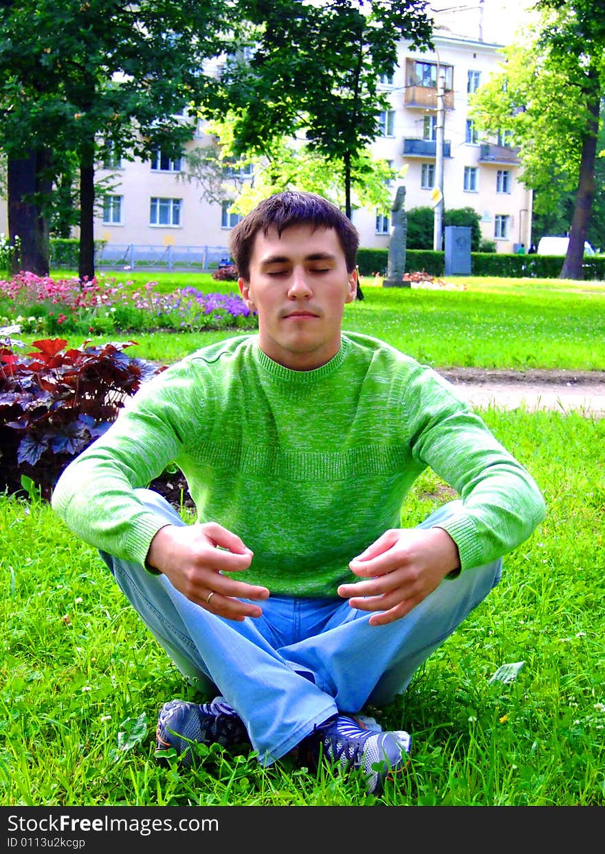 Photo of the young man meditating on a grass.