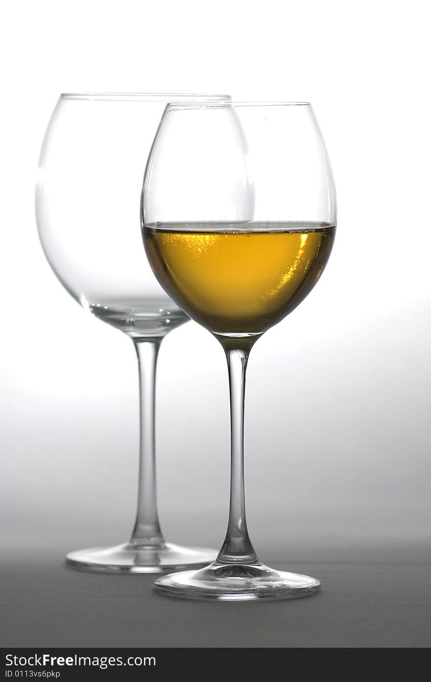 Two tall wine glasses on light background, one filled with white wine