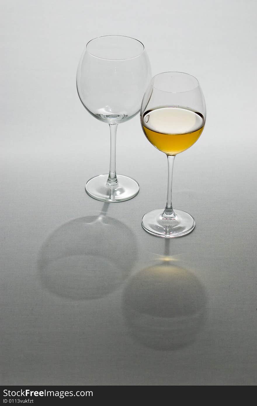 Two tall wine glasses on light background, one filled with white wine