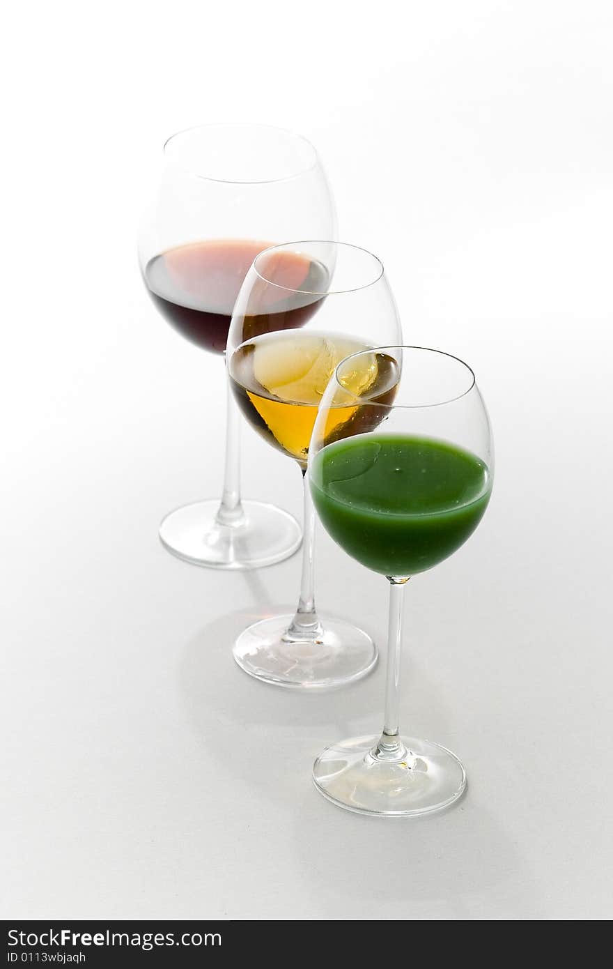 Three tall glasses on white background filled with: white, red wine and green cocktail