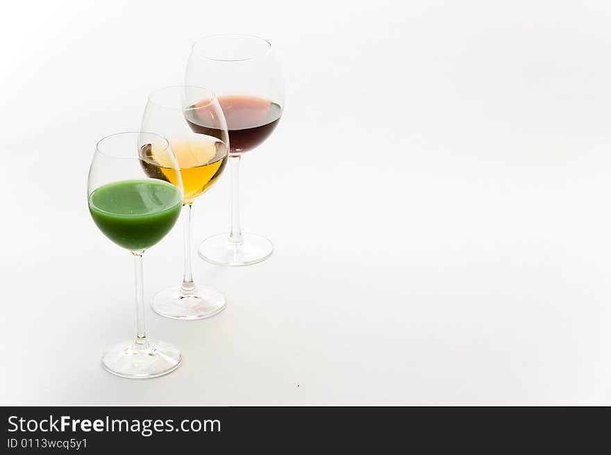 Three tall glasses on white background filled with: white, red wine and green cocktail