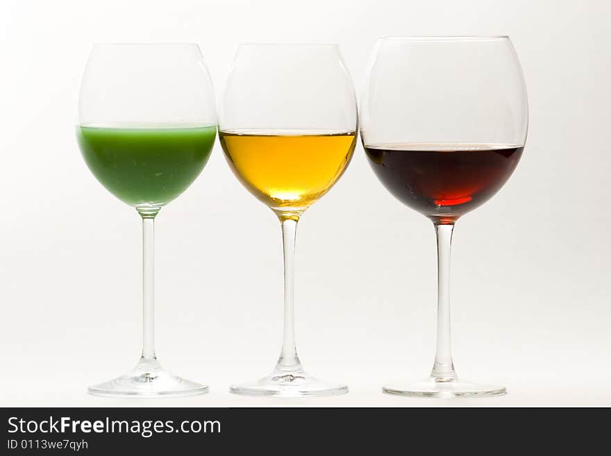 Three tall glasses on white background filled with: white, red wine and green cocktail