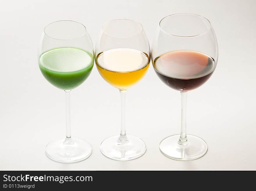 Three tall glasses on white background filled with: white, red wine and green cocktail