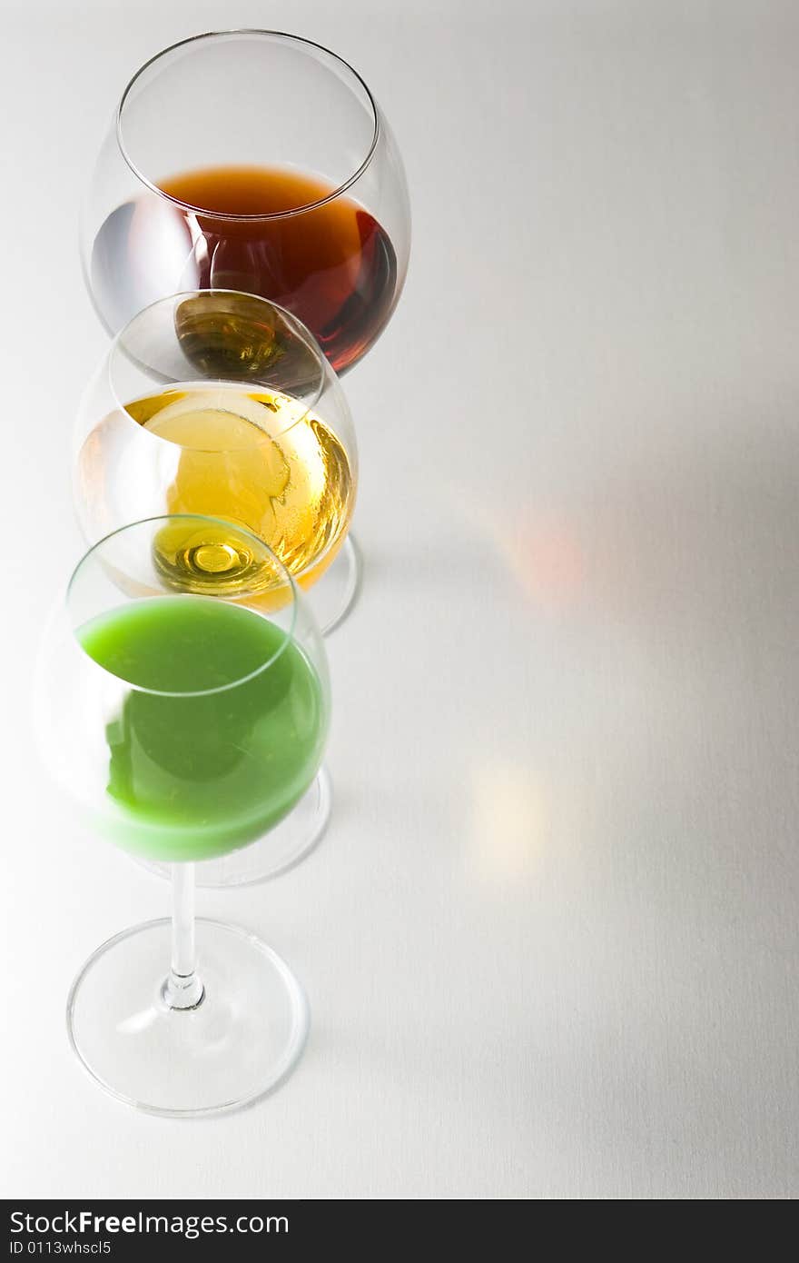 Three tall glasses on white background filled with: white, red wine and green cocktail