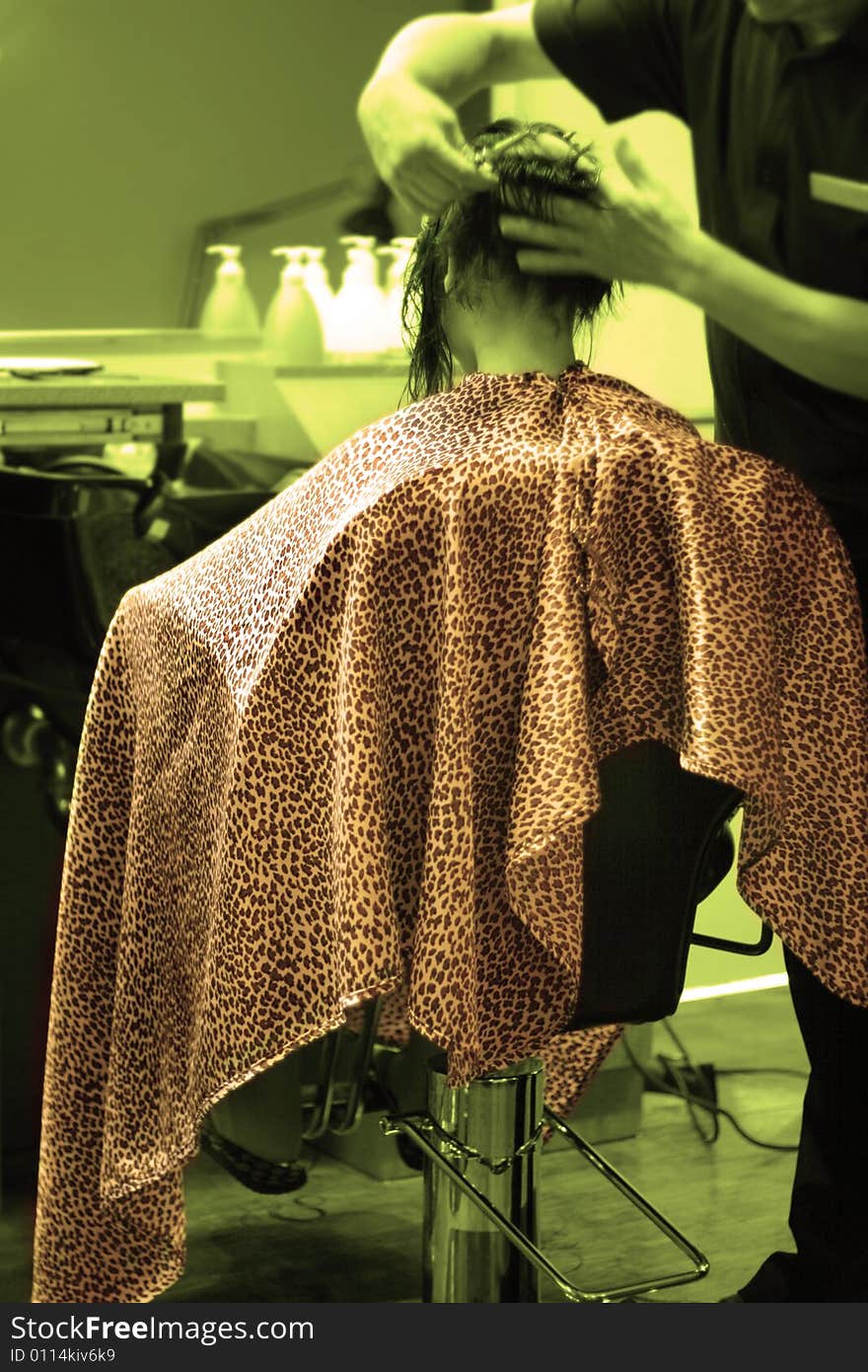 Girl seating in a salon chair with robe, getting a haircut; selective coloring