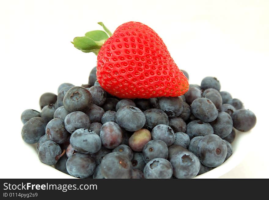 An image of a strawberry on top of a bowl full of fresh blueberries. An image of a strawberry on top of a bowl full of fresh blueberries.