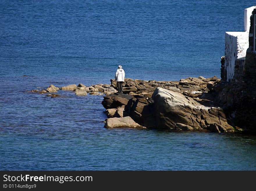 An elderly man standing on the rocks by the surf. An elderly man standing on the rocks by the surf.