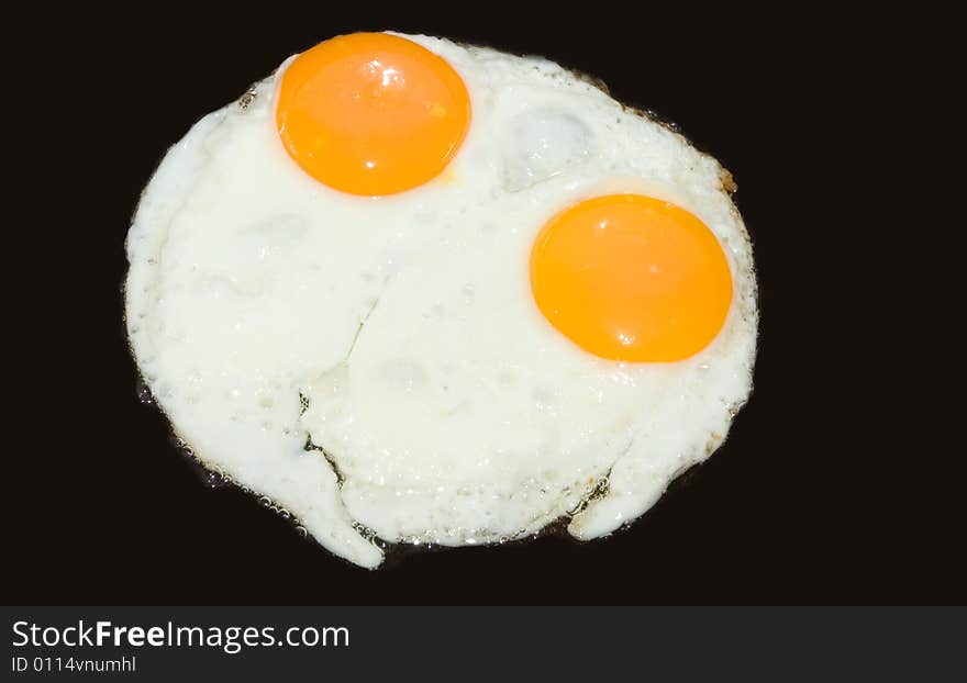 A pair of eggs being cooked. isolated on black.