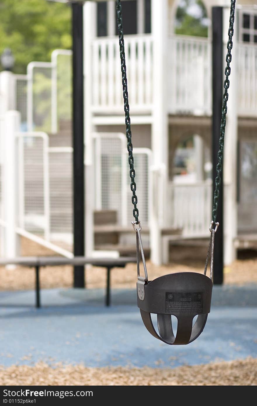 Infant swing on playground in foreground, play equipment out of focus in background