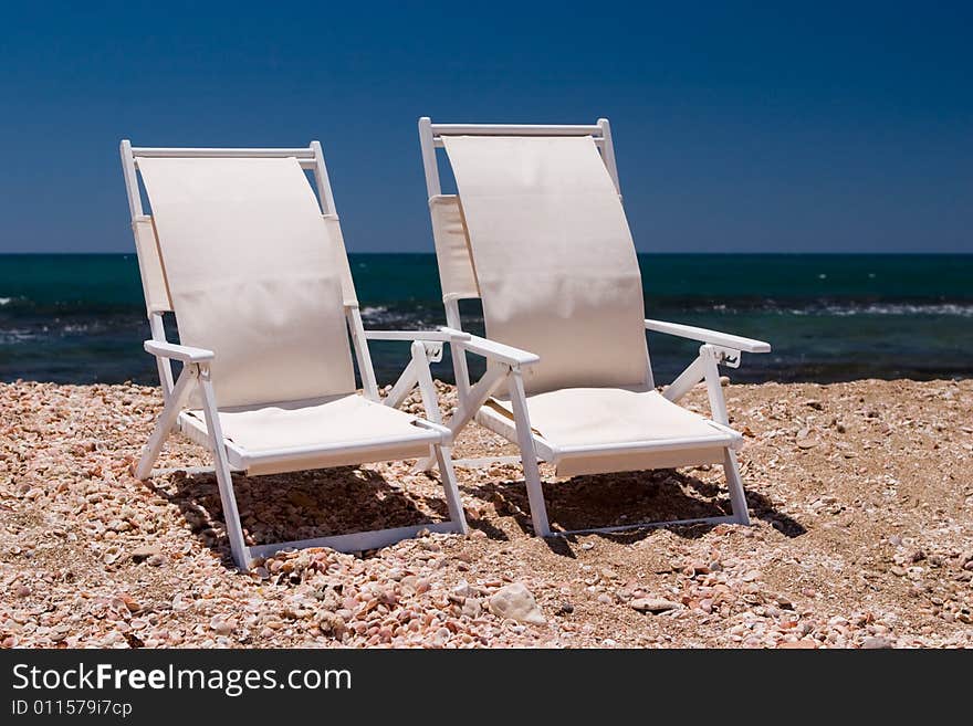 Two white chairs on a beach with sea shell and sand