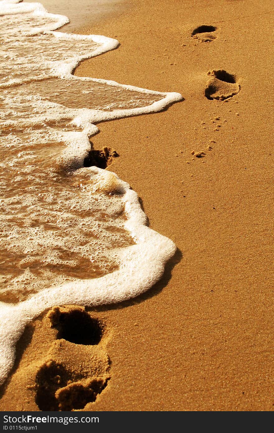 Footprints in the sand beeing washed away by a wave. Footprints in the sand beeing washed away by a wave