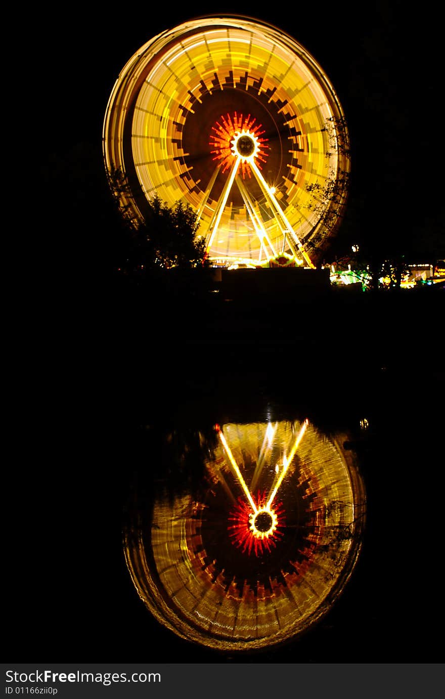 Ferris wheel at night at Ulm's folk festival with its reflection on a water surface.