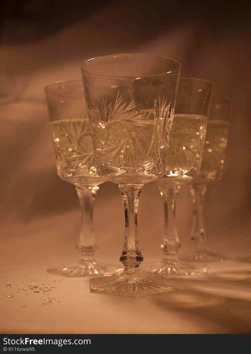 Four decorated glasses with white wine and some spilled wine on orange warm background