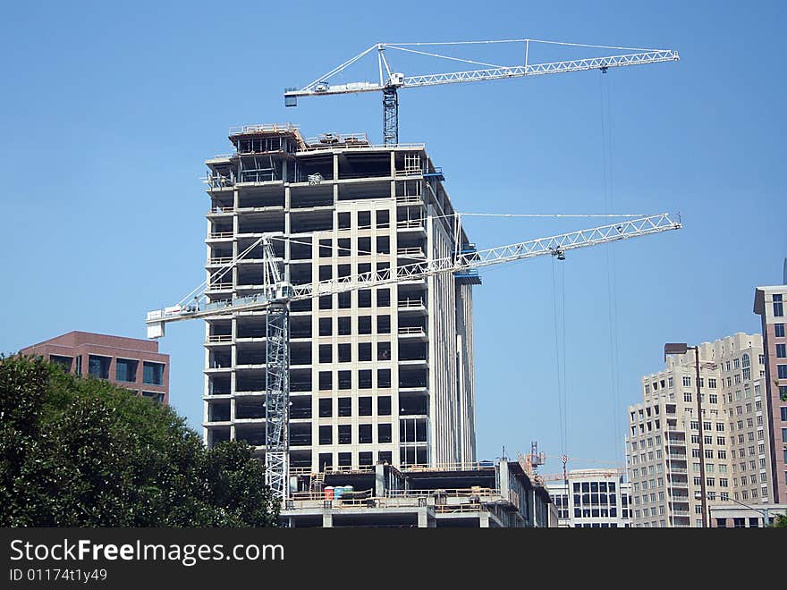 Two cranes are in the foreground of the construcion of a large building. Two cranes are in the foreground of the construcion of a large building