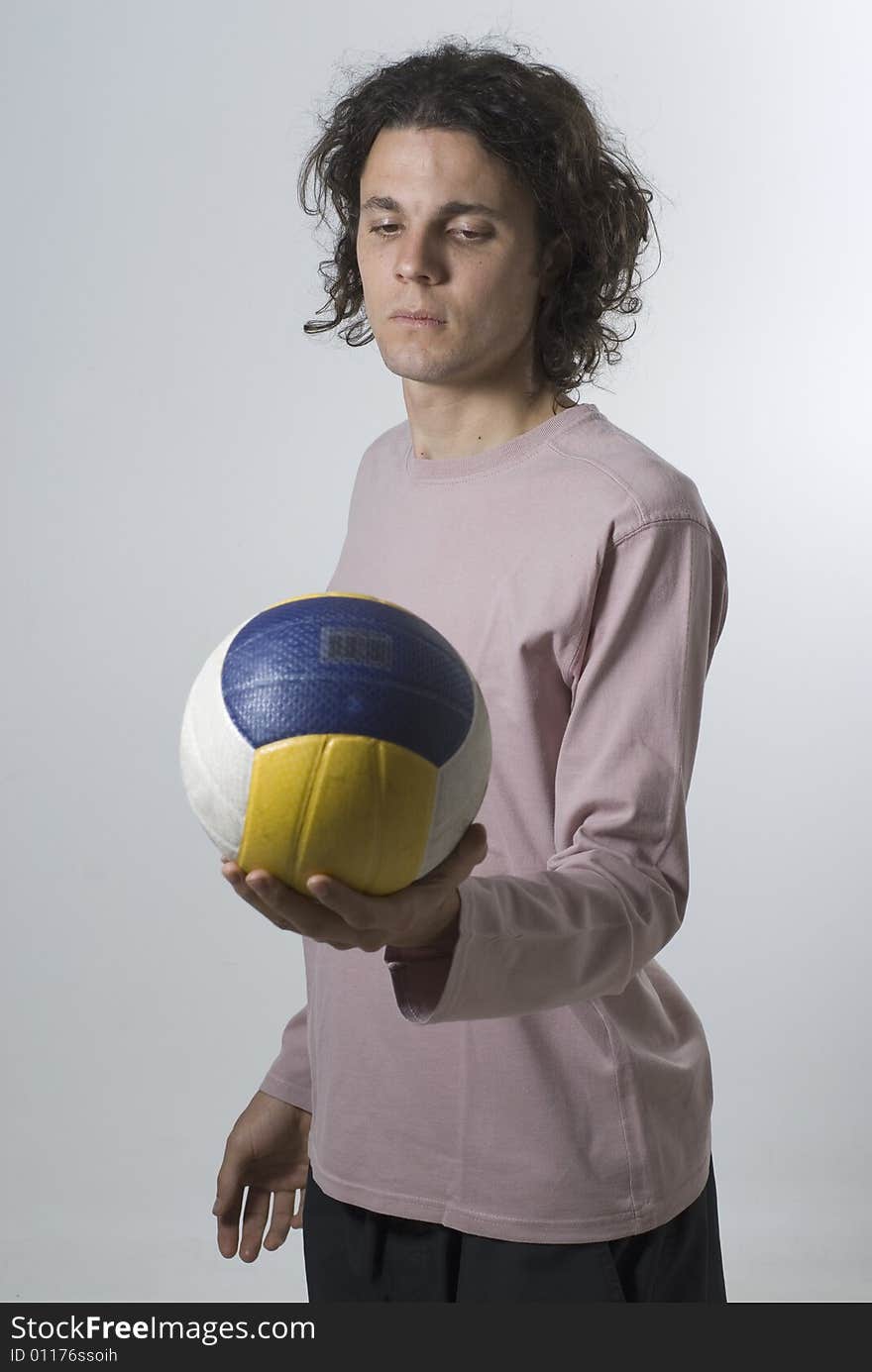 Man holds a volleyball and stares at it with a serious expression on his face.  Vertically framed photograph. Man holds a volleyball and stares at it with a serious expression on his face.  Vertically framed photograph