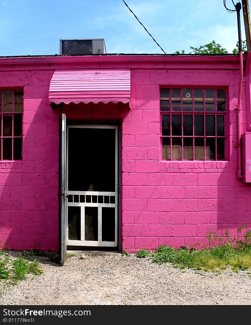 A view of the front of a bright pink building.  There is a door and windows.  Vertically framed shot. A view of the front of a bright pink building.  There is a door and windows.  Vertically framed shot.