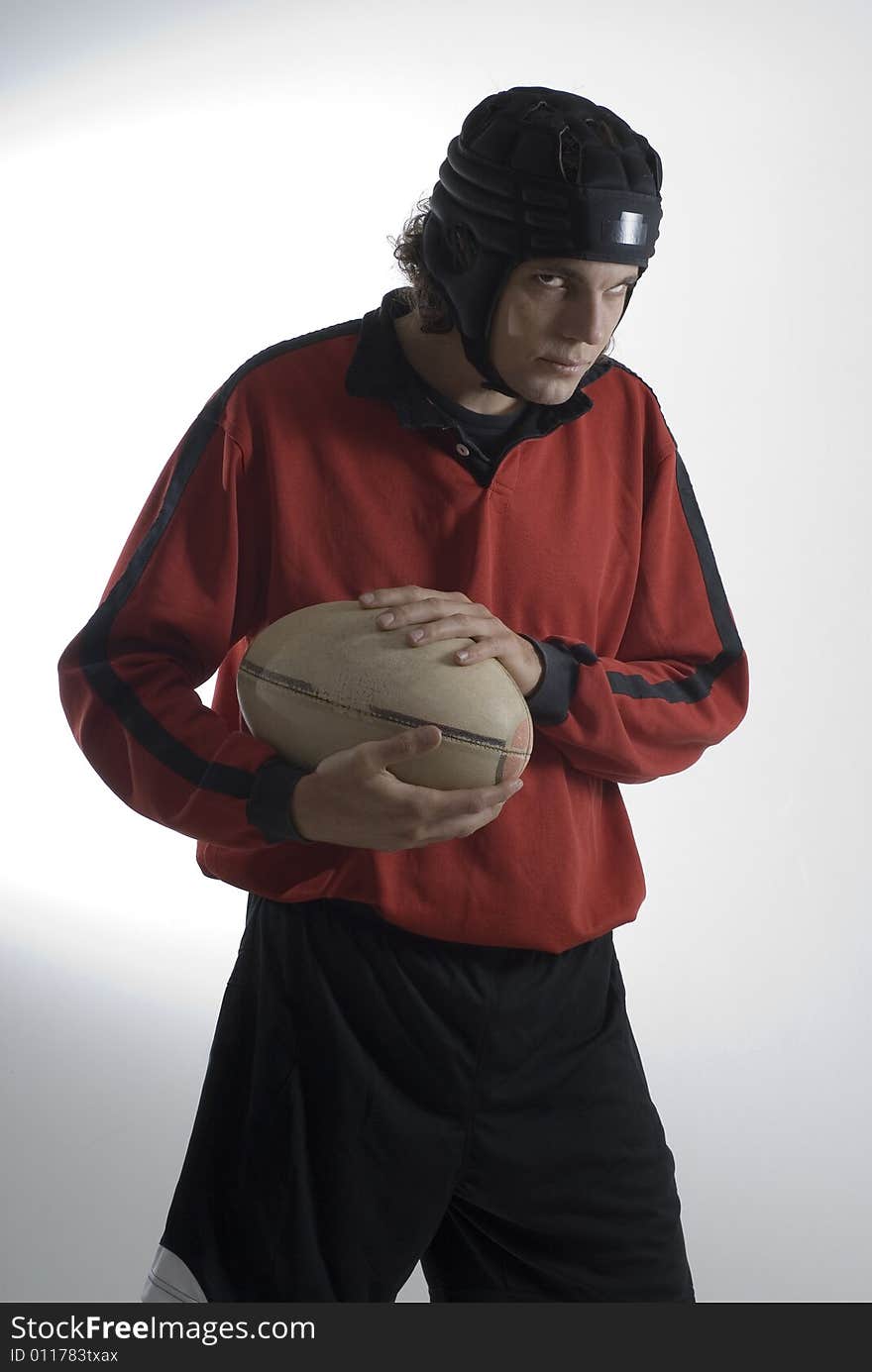 Rugby player wearing a helmet and uniform holds a football and has a sullen look on his face. Vertically framed photograph. Rugby player wearing a helmet and uniform holds a football and has a sullen look on his face. Vertically framed photograph