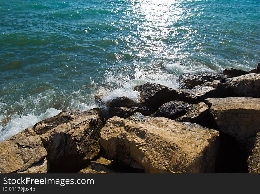 Waves on stones at the beach with sun reflecting in the water