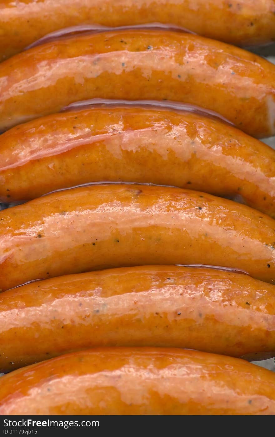 Sausages being grilled and smothered with barbecue sauce.