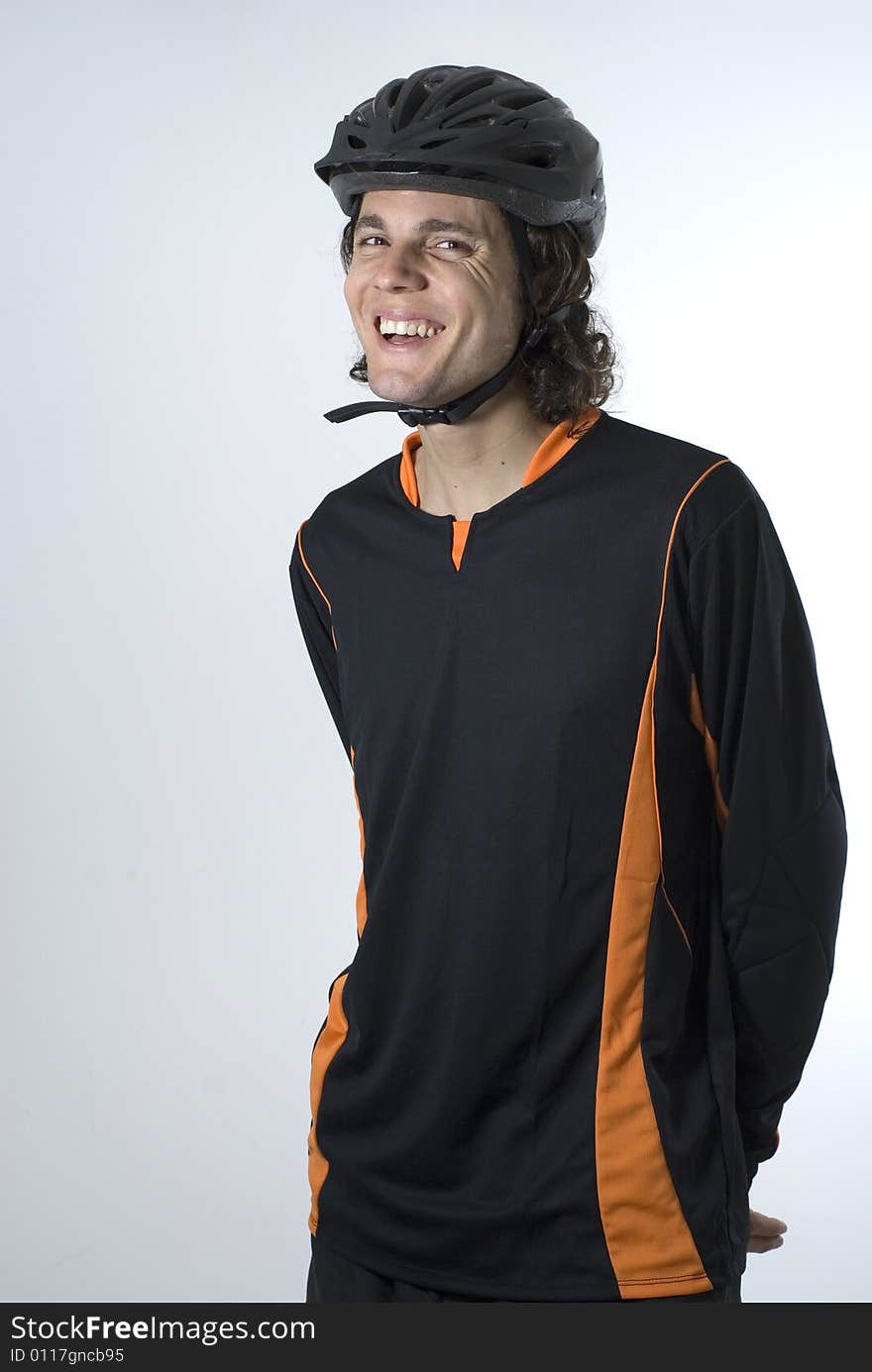 A man stands in a black and orange biking outfit and helmet, smiling at the camera. Vertically framed shot. A man stands in a black and orange biking outfit and helmet, smiling at the camera. Vertically framed shot.