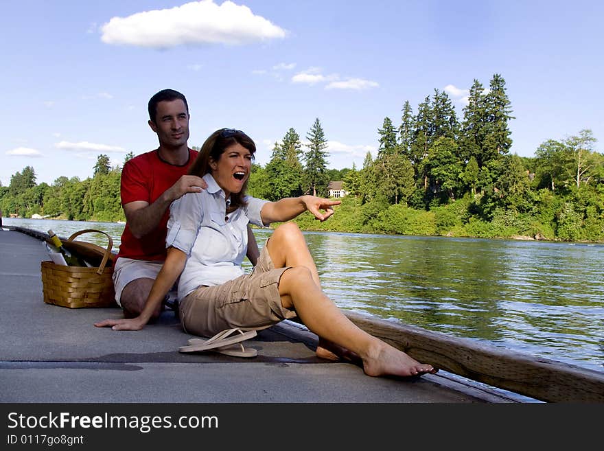 Happy couple laughing as they relax by the lake with a picnic basket next to them. Vertically framed photograph. Happy couple laughing as they relax by the lake with a picnic basket next to them. Vertically framed photograph