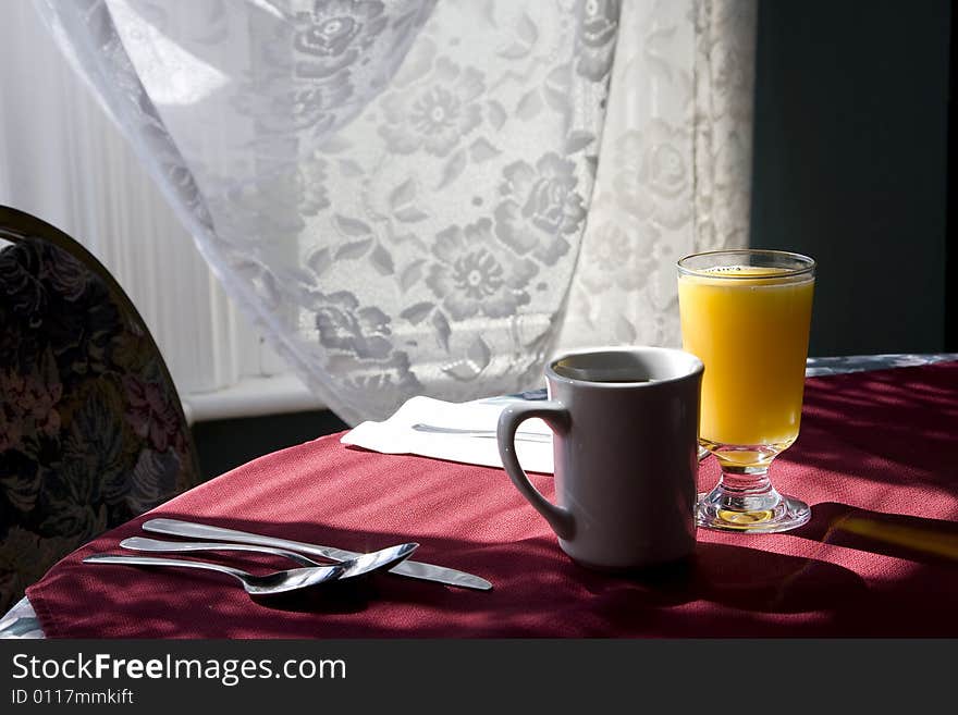 Glass of orange juice and cap of coffee on a table chair highlighted by the sunlight from  the window. Glass of orange juice and cap of coffee on a table chair highlighted by the sunlight from  the window.